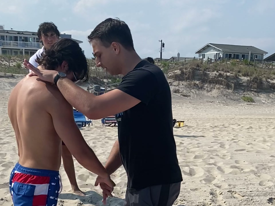 Tyler guiding a beach demonstration beside a participant with their head lowered.